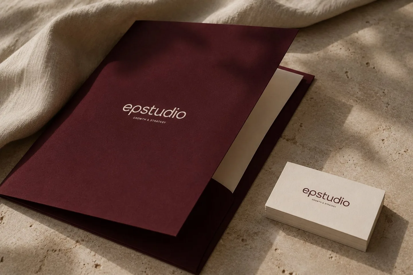 Carpeta granate y tarjetas de EP Studio sobre piedra travertino